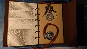 A journal turned to the last pre-printed page which contains a character's detailed backstory, and the journal's personalized charms and trinkets on the place marker and string closure.