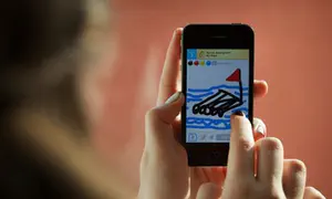 Player holding up a phone with the 'Draw Something' app loaded.